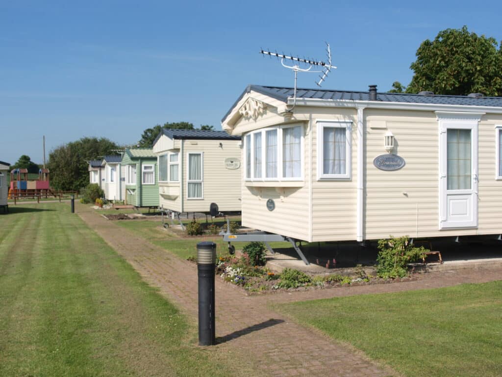 Row of static caravans lined up on a well-kept holiday park, with grassy surroundings and clear skies overhead.