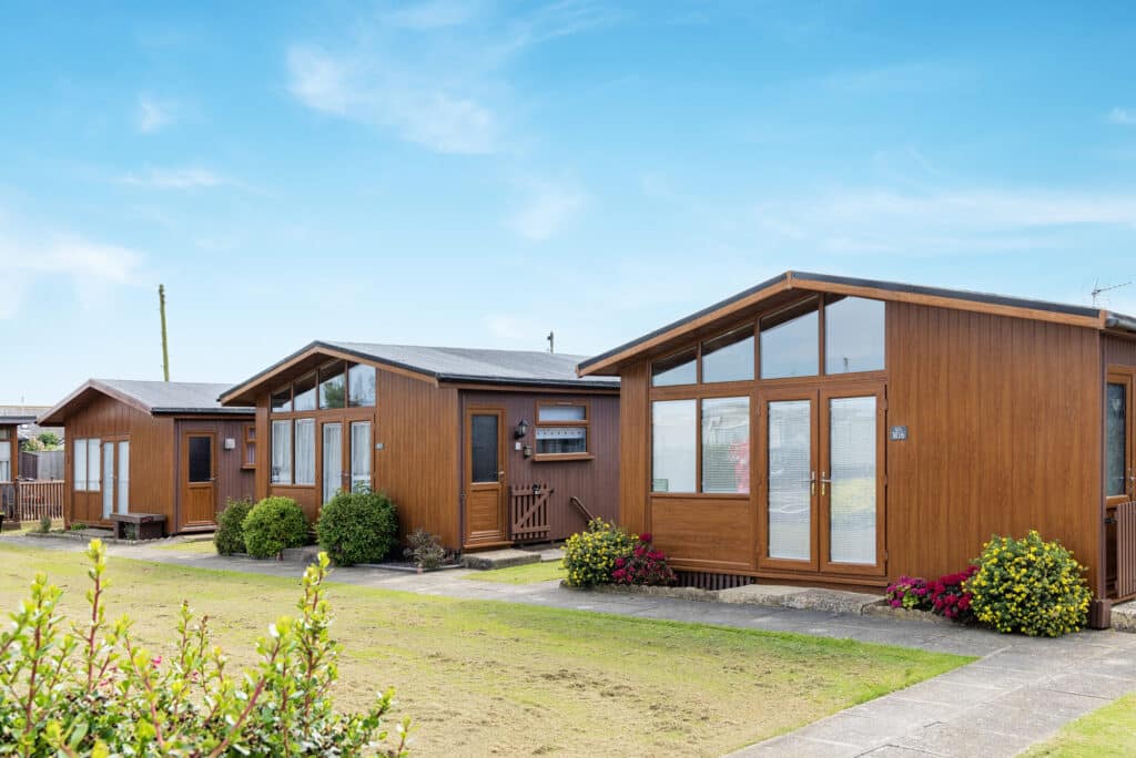 Row of holiday chalets with individual entrances, set in a landscaped park with pathways and greenery.