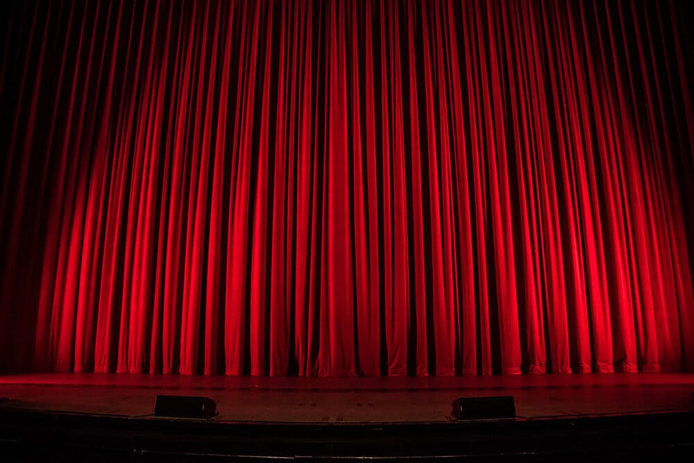 Rich red theatre curtains drawn closed on a stage, evoking a classic and dramatic atmosphere.
