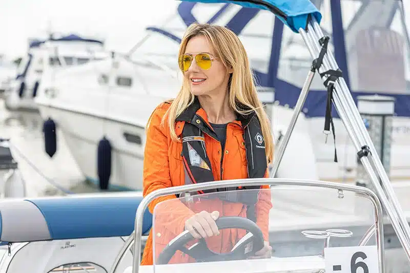 Happy woman on boat with hands on the wheel.