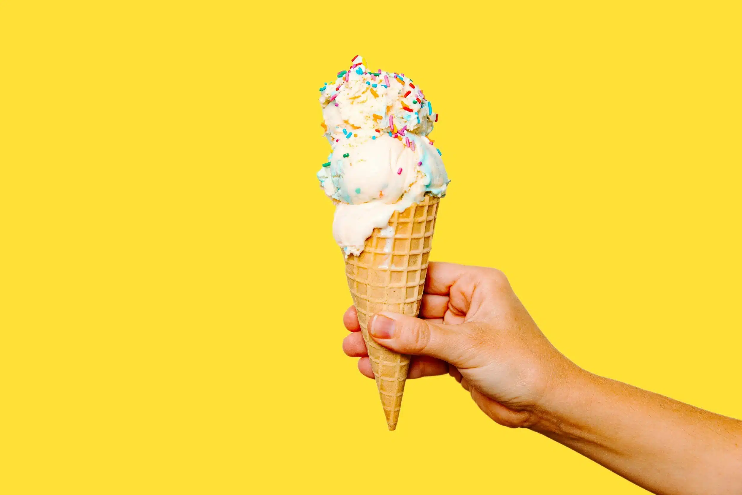 Hand holding a two-scoop vanilla ice cream cone topped with colourful sprinkles