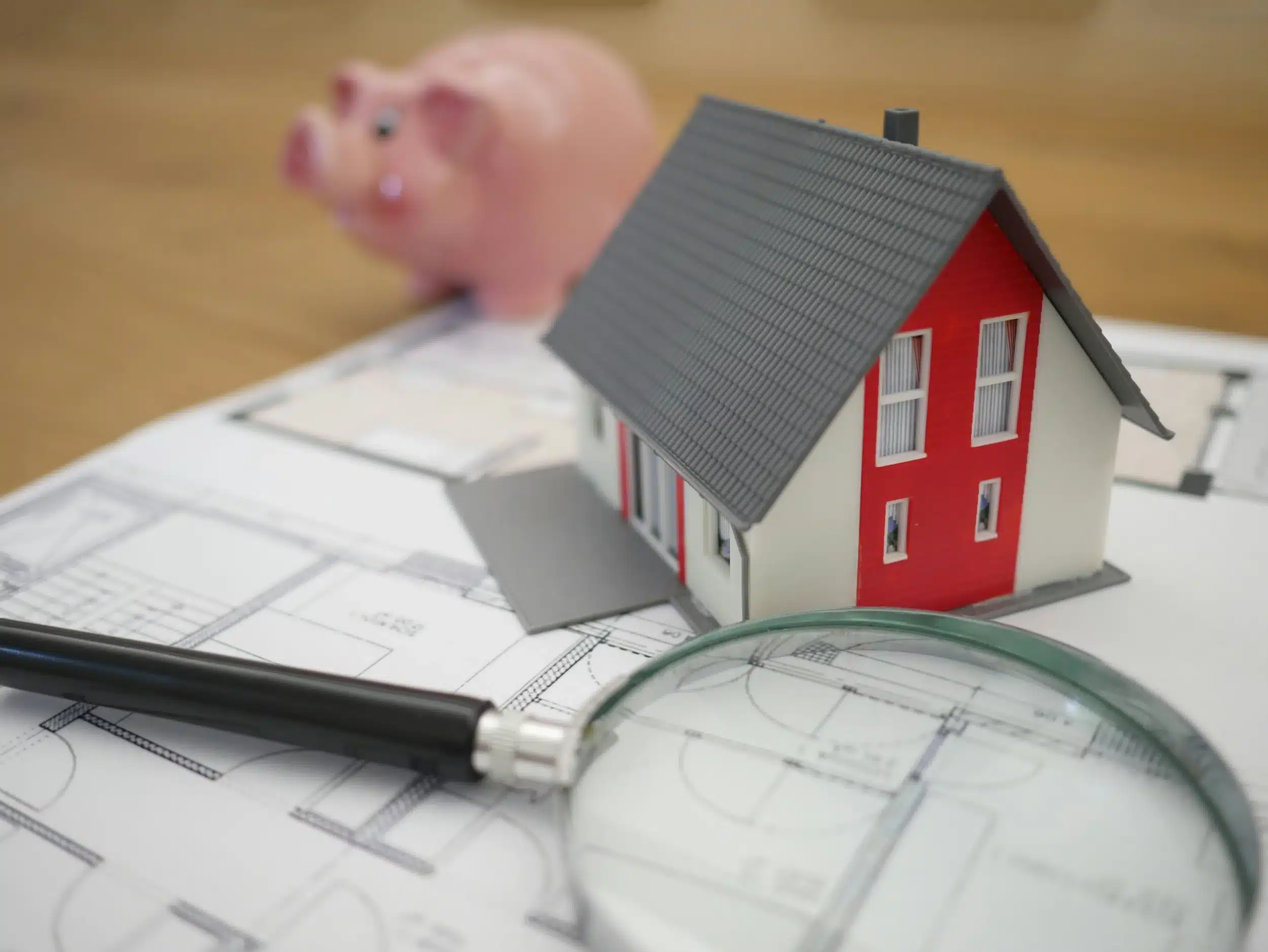 Small piggy bank, miniature house, and magnifying glass on a floor plan