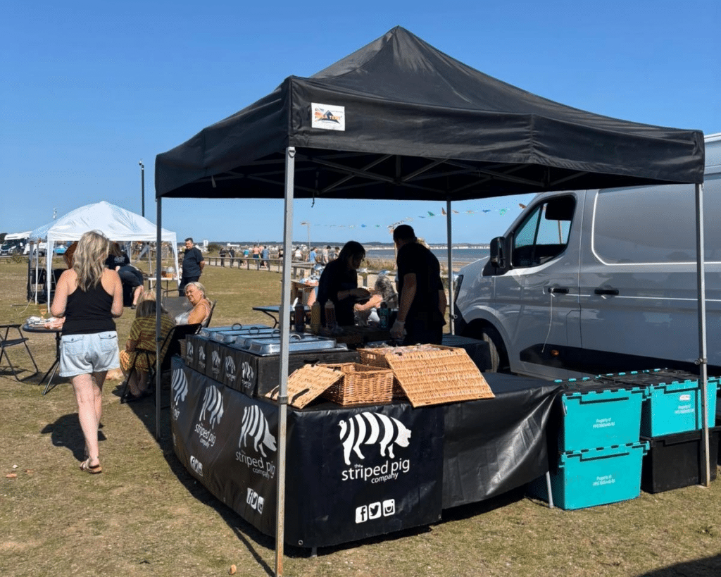 Save the dates for our upcoming events at South Shore Park 2 We are sharing an image of one exa,ple of our upcoming events at South Shore Park. It's a group of people stands under a tent surrounded by boxes and bottles, engaged in conversation and activity.